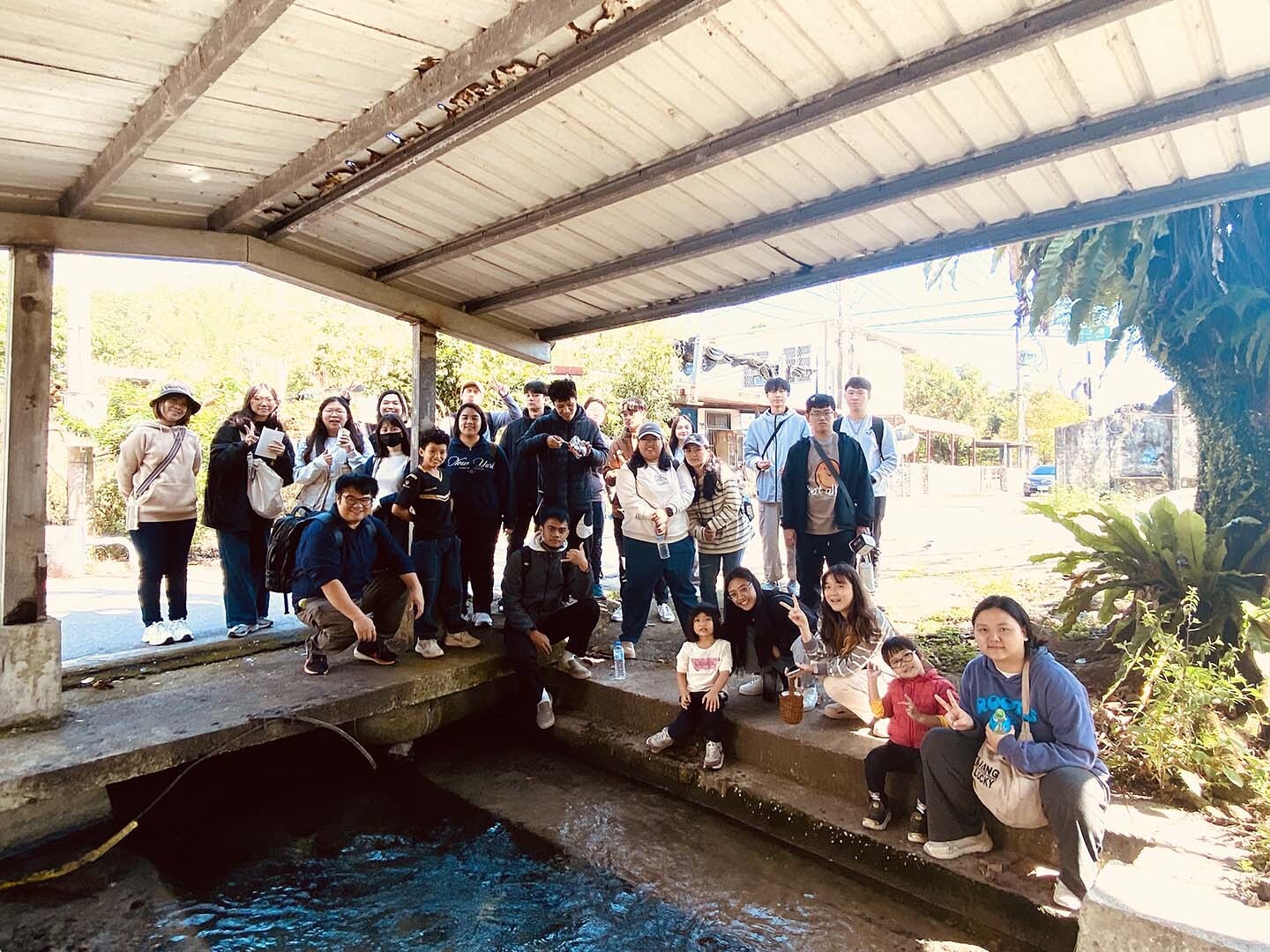 學生於社區水圳和洗衣亭下合影,體驗部落文化場域的感知與互動