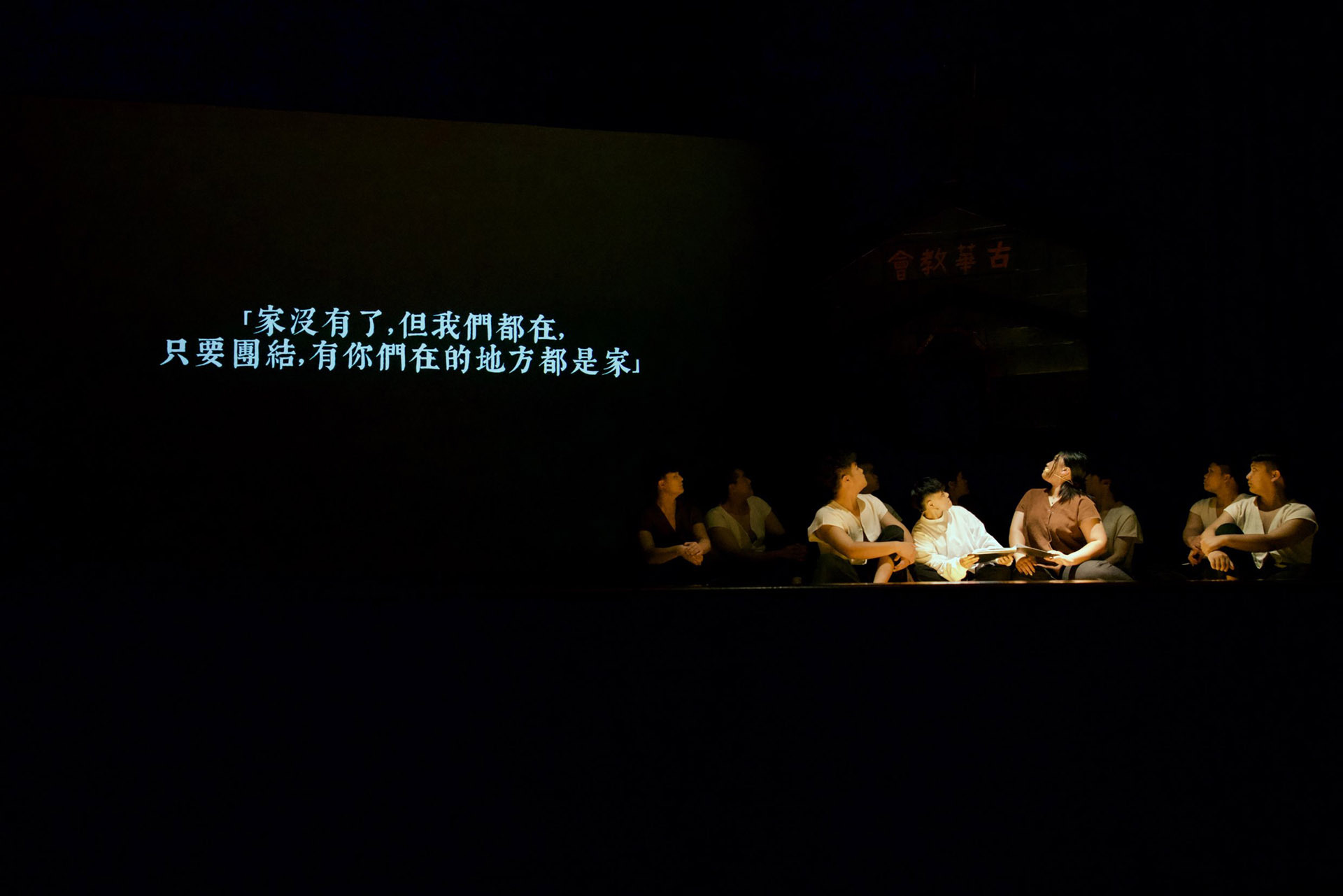 行動藝術《聚 離》表演者在舞台上圍坐一圈,投影字幕寫著:「家沒有了,但我們都在,只要團結,有你們在的地方都是家」,傳遞出災後重建與團結互助的核心理念