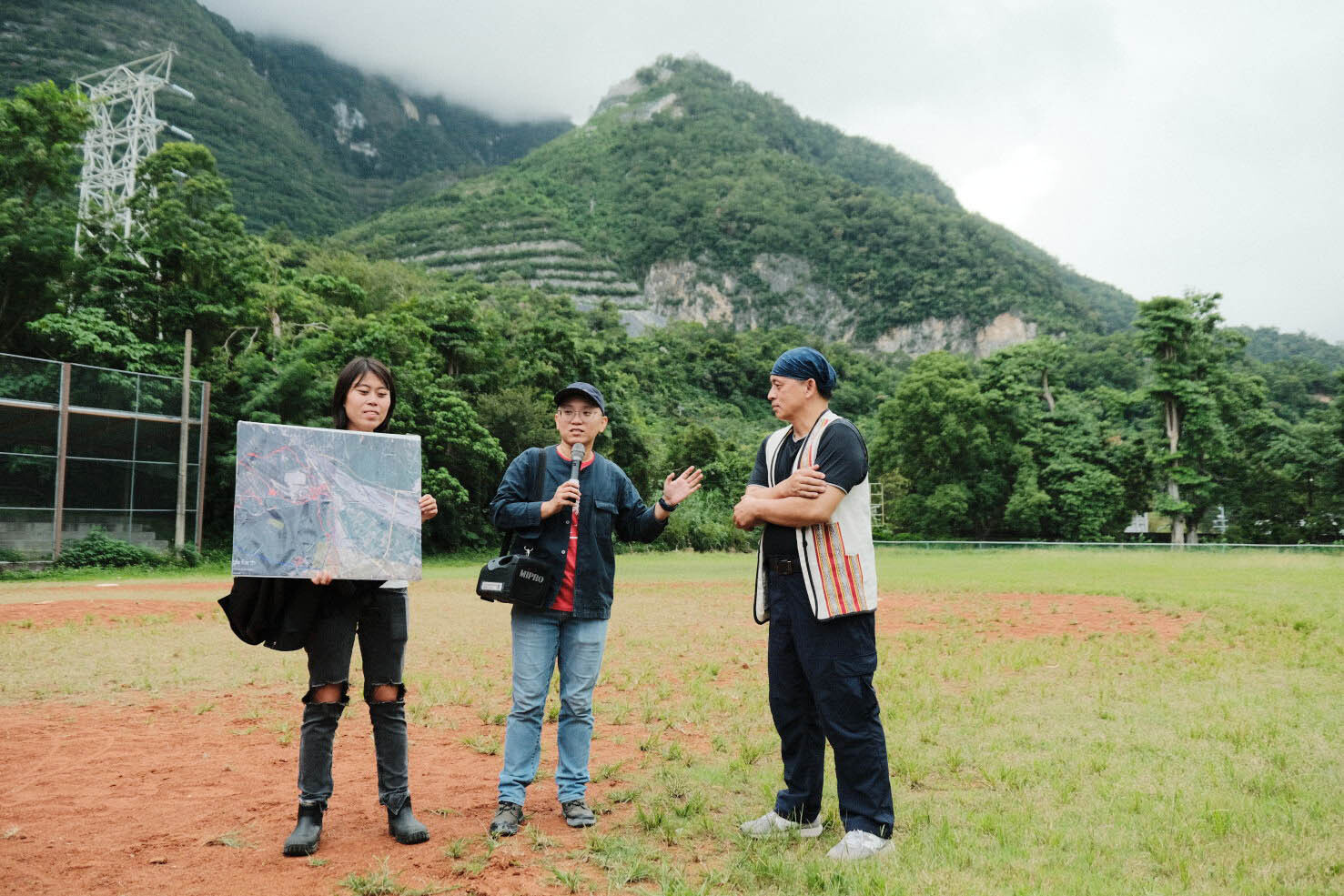 地球公民基金會教育專員劉思怡(左)、地球公民基金會副執行長黃靖庭(中)與反亞泥自救會環保人士白誠實(右)於壘球場講解居住在礦區下的富世村。背後如梯田般的山就是亞泥開採後的礦區